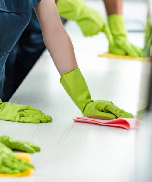 cropped view of cleaners in rubber gloves cleaning office desk