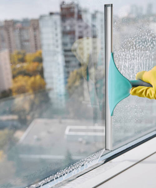 Gloved hand washing windowpane using implement with rubber blade